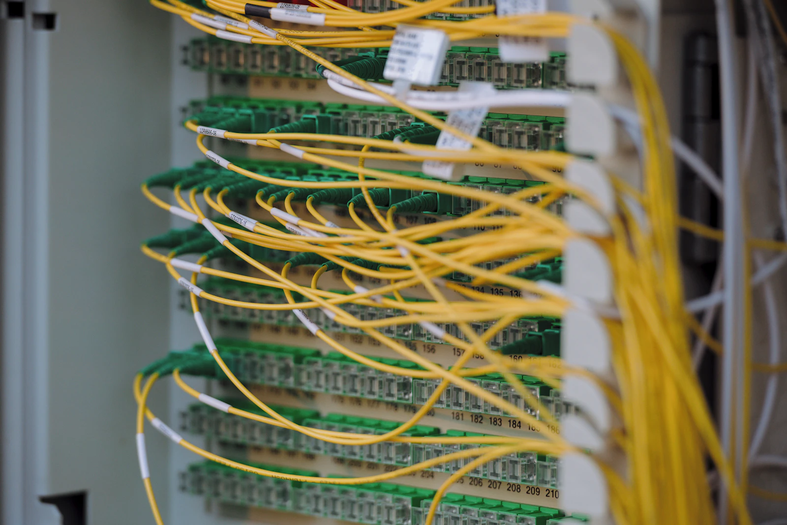 Yellow fibre-optic patch cables plugged into rows of green connectors on a numbered fibre distribution panel