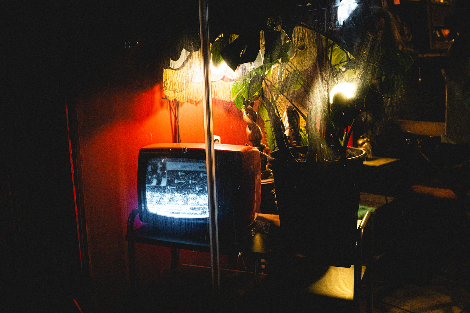 Small vintage television glowing with a grainy black-and-white picture in a dark room lit by a red wall and lamp