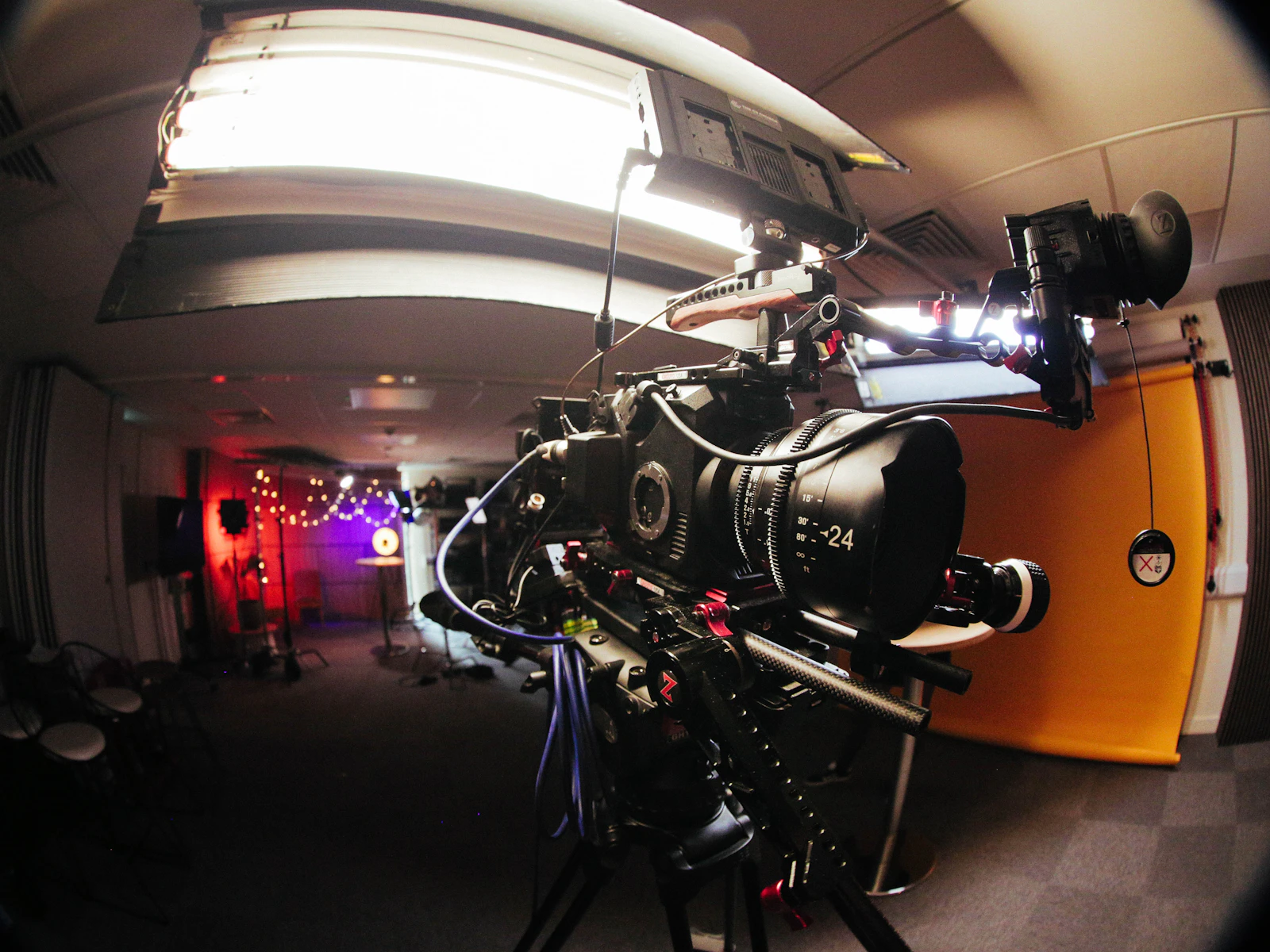 Rigged cinema camera with a 24mm prime lens and viewfinder on a tripod in a film studio under a large soft light